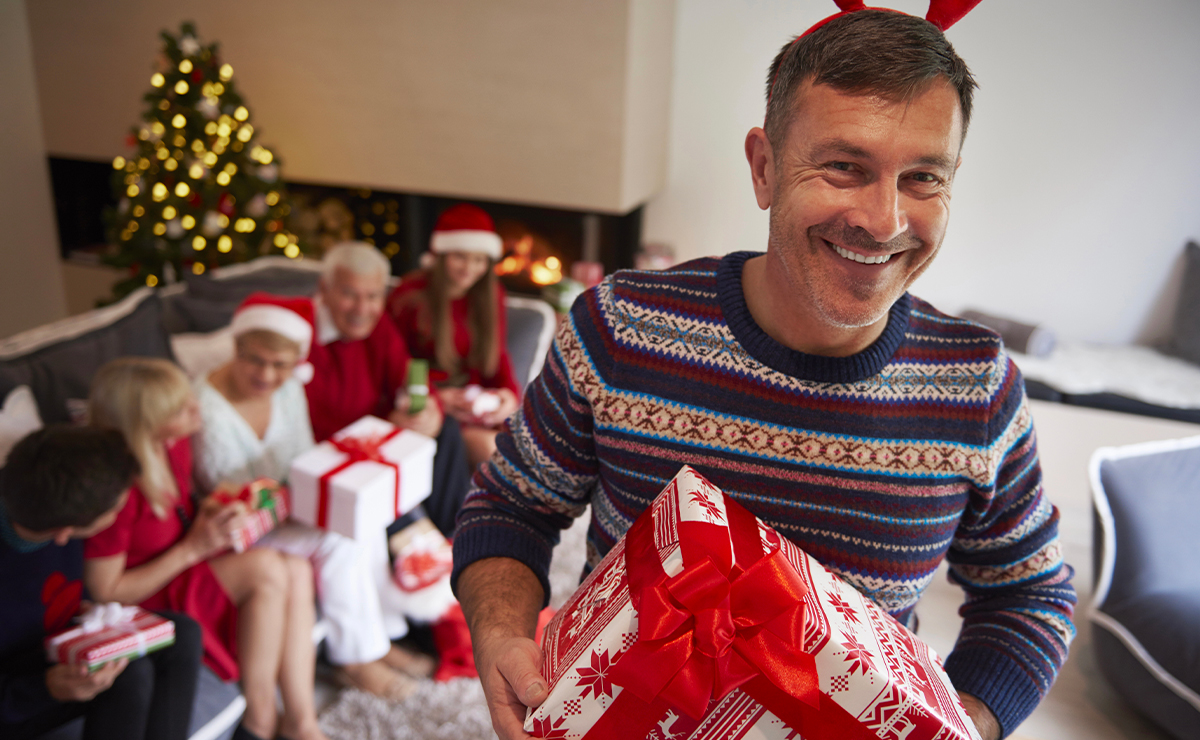 Uomo sorridente con maglione natalizio e cerchietto da renna tiene in mano un regalo