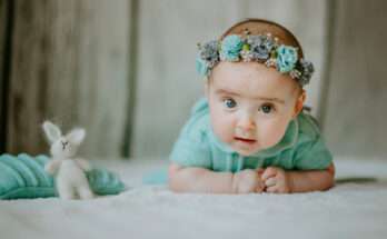 Bambina sdraiata a pancia in giù con fascia di fiori azzurri e vestitino verde acqua