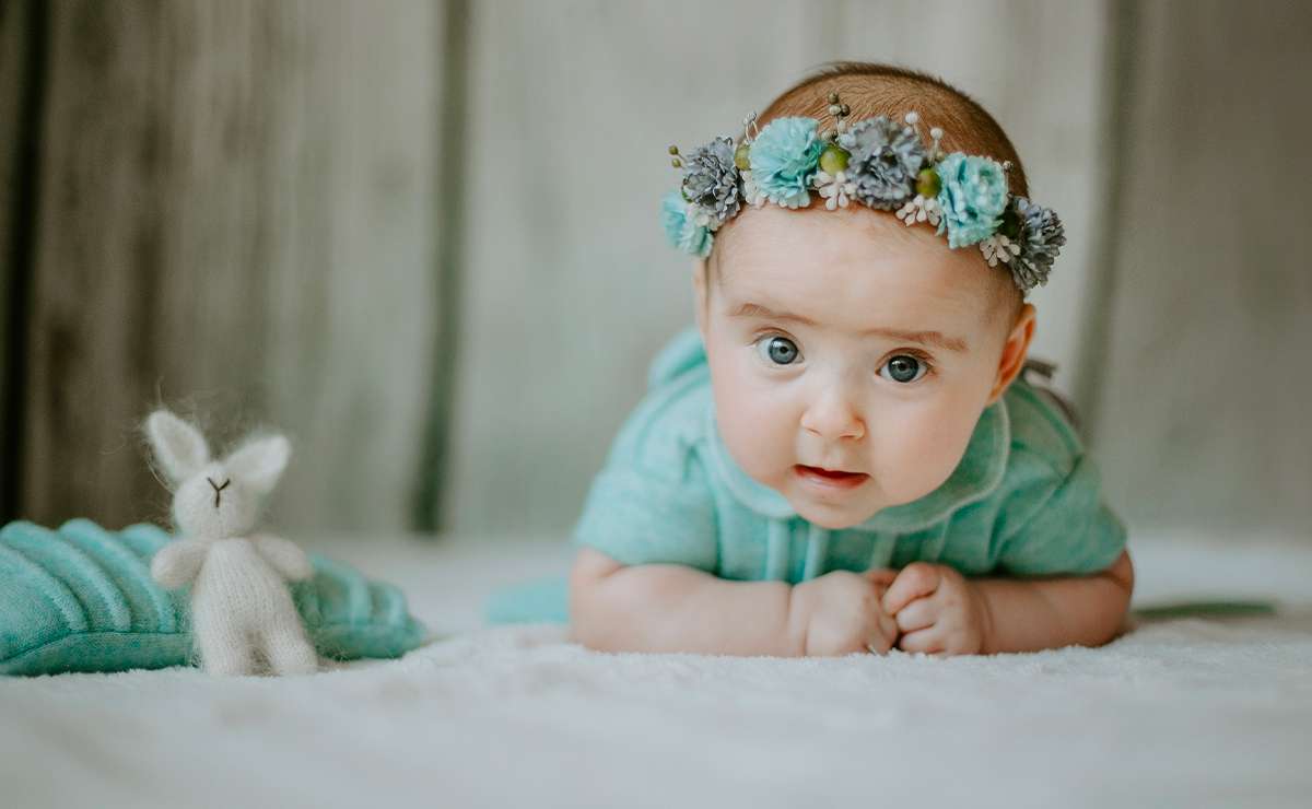 Bambina sdraiata a pancia in giù con fascia di fiori azzurri e vestitino verde acqua