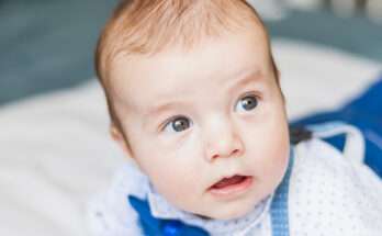 Bambino con camicia chiara e bretelle blu che guarda incuriosito verso l’alto