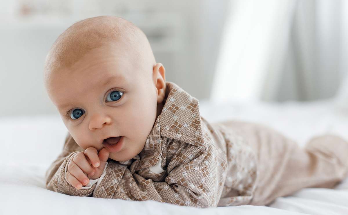 Bambino sdraiato su un letto bianco con occhi azzurri e completo beige