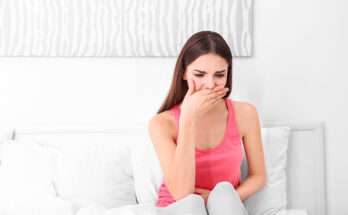 Donna seduta sul letto che copre la bocca con la mano per nausea