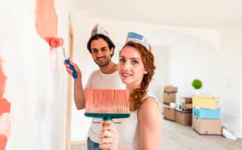 Coppia che ridipinge una parete di casa con rullo e pennello