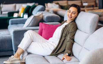 Donna seduta su un divano moderno grigio chiaro con schienale alto, in showroom arredamento, mentre testa la comodità del modello