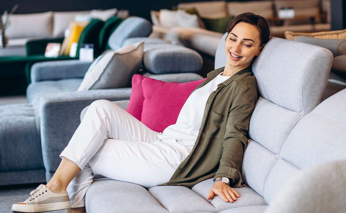 Donna seduta su un divano moderno grigio chiaro con schienale alto, in showroom arredamento, mentre testa la comodità del modello