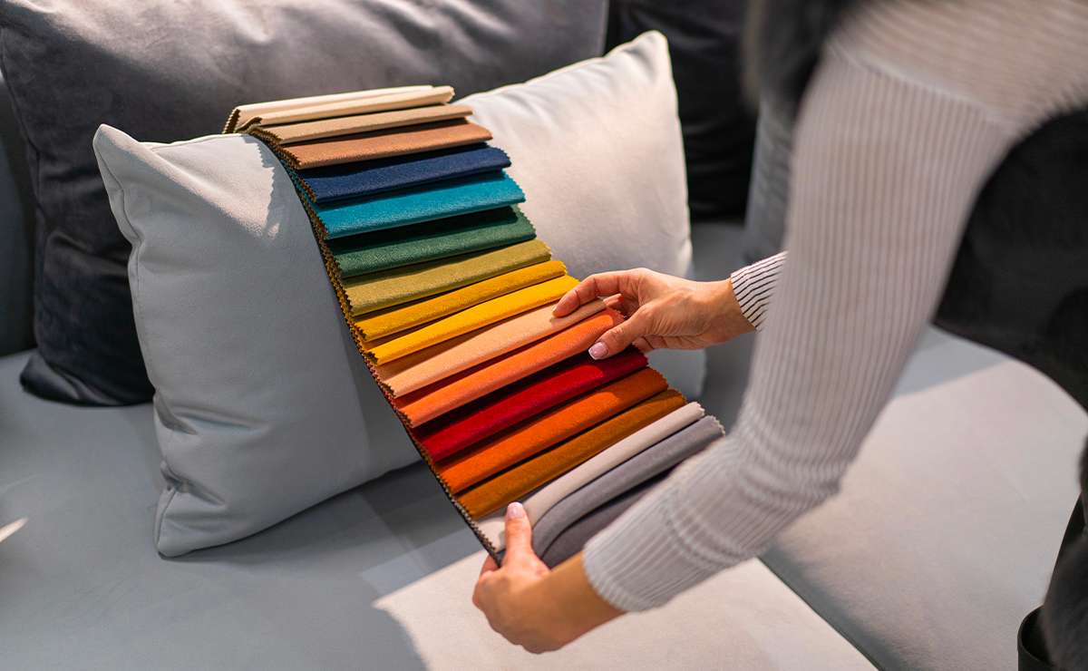 Campionario di tessuti colorati per rivestimento divani, appoggiato su un cuscino chiaro mentre una persona sceglie il colore più adatto
