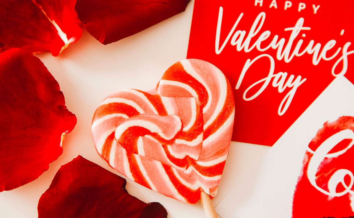 Lollipop a forma di cuore rosso e bianco su sfondo con petali di rosa e cartoline di San Valentino.
