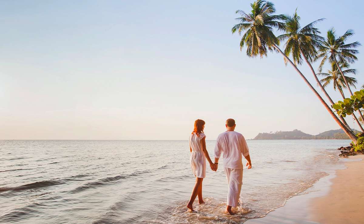 Coppia che cammina mano nella mano sulla riva del mare al tramonto