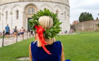 Laureata di spalle con corona d’alloro e abito blu seduta sul prato