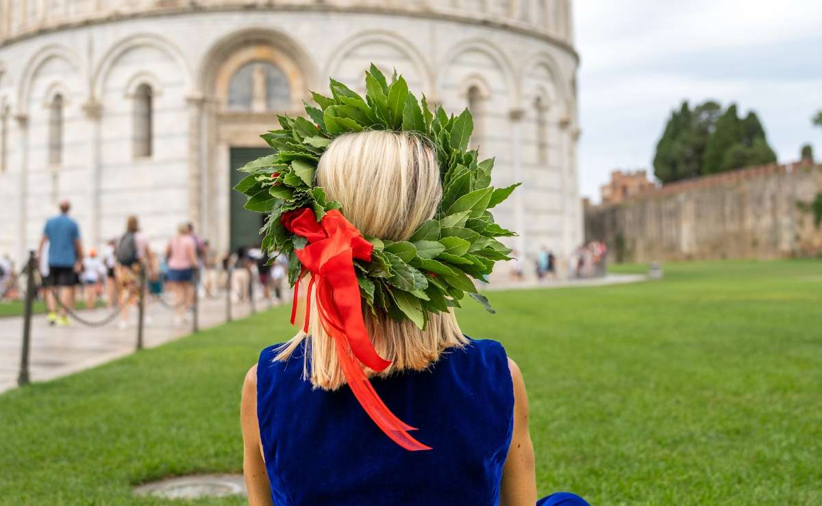 Laureata di spalle con corona d’alloro e abito blu seduta sul prato