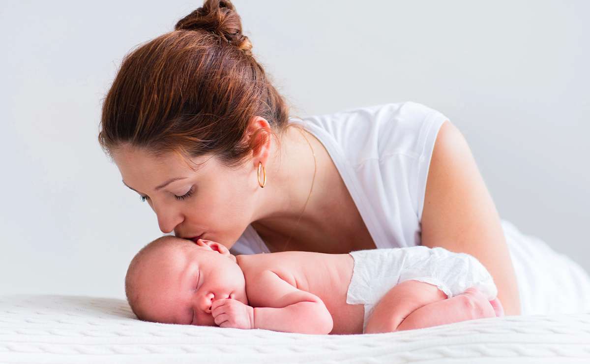 Madre che bacia dolcemente il neonato addormentato, sdraiato su una coperta chiara