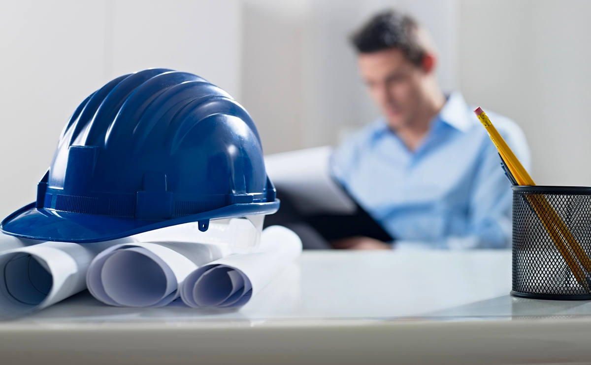 Casco da cantiere blu appoggiato su rotoli di progetti edilizi su una scrivania