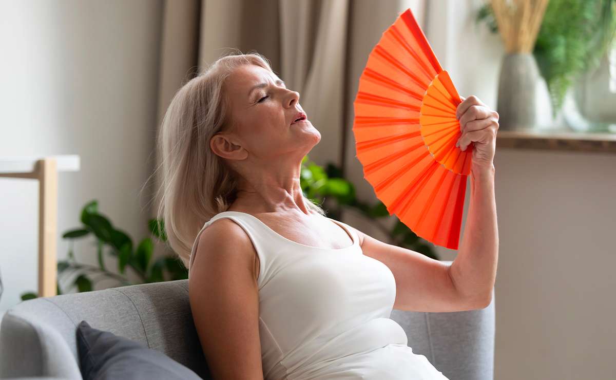 Donna in menopausa seduta sul divano mentre si rinfresca con un ventaglio arancione