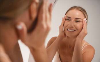 donna sorridente davanti allo specchio mentre massaggia il viso