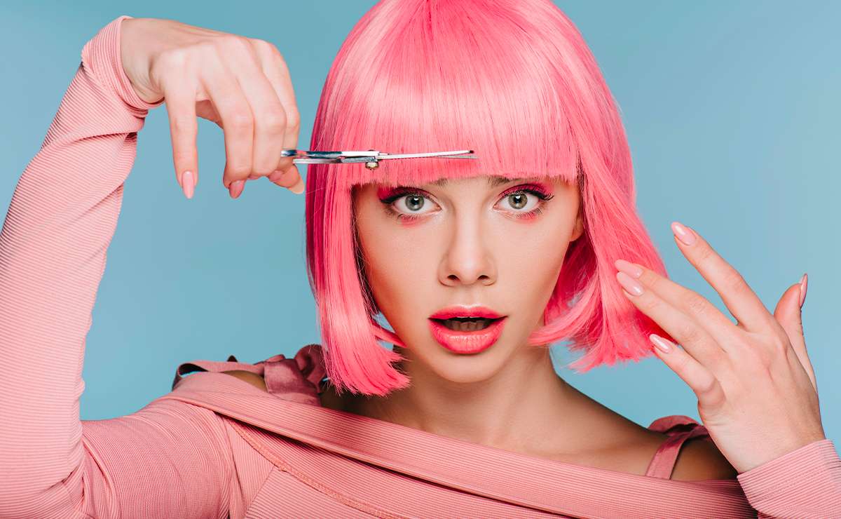 Donna con parrucca rosa acceso che si taglia la frangia con una forbice