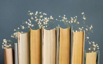 Libri con pagine ingiallite disposti in fila, decorati con piccoli fiori bianchi tra le copertine