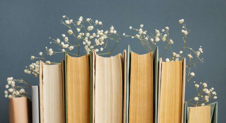 Libri con pagine ingiallite disposti in fila, decorati con piccoli fiori bianchi tra le copertine