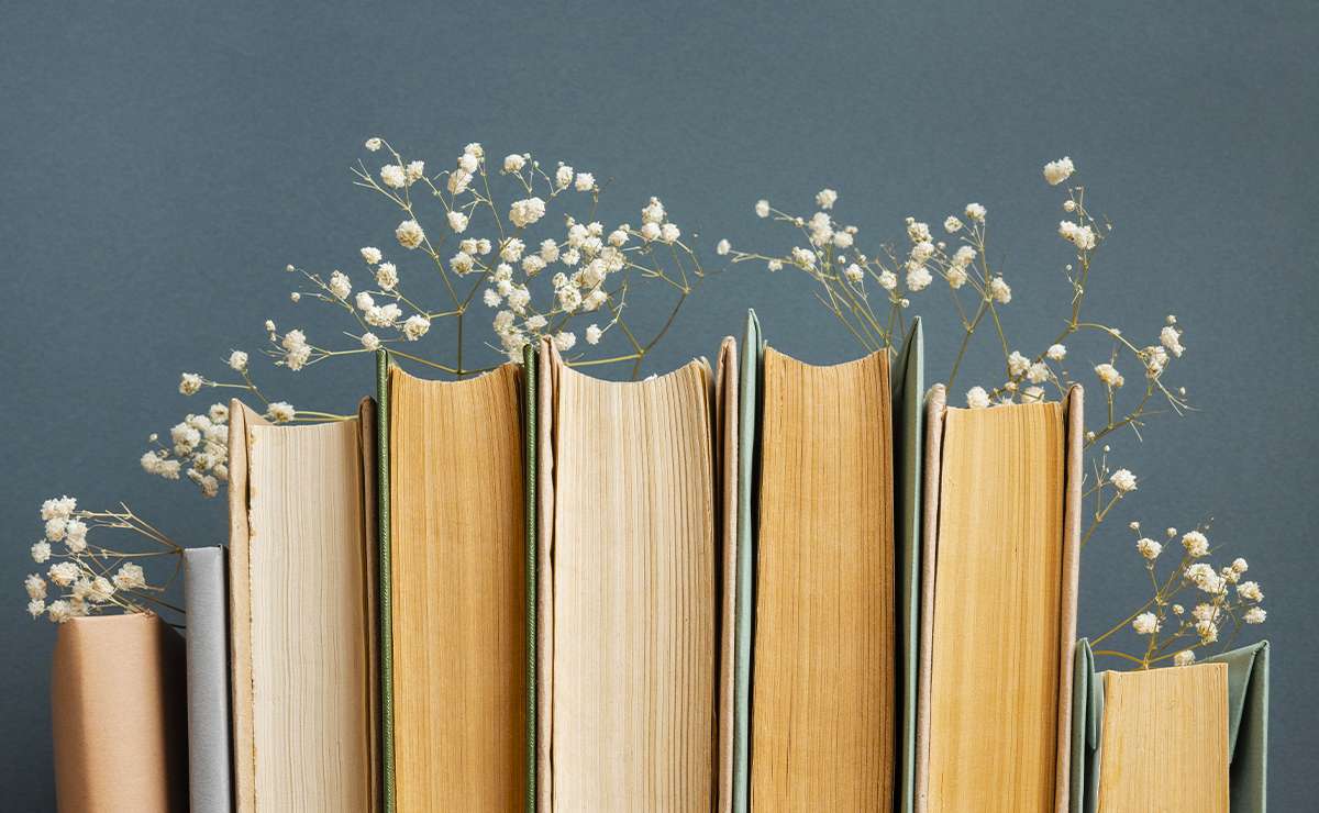 Libri con pagine ingiallite disposti in fila, decorati con piccoli fiori bianchi tra le copertine