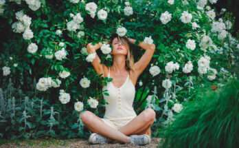 Donna seduta in giardino circondata da rose bianche in piena fioritura