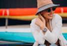 Donna con blazer chiaro, cappello beige e occhiali da sole indossa un orologio da polso elegante