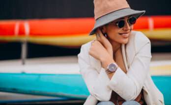 Donna con blazer chiaro, cappello beige e occhiali da sole indossa un orologio da polso elegante