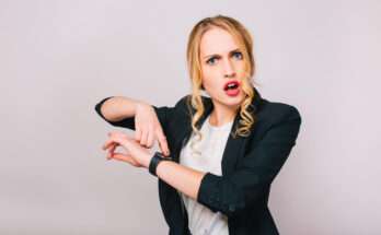 donna bionda indica l'ora sull'orologio da polso con espressione stupita