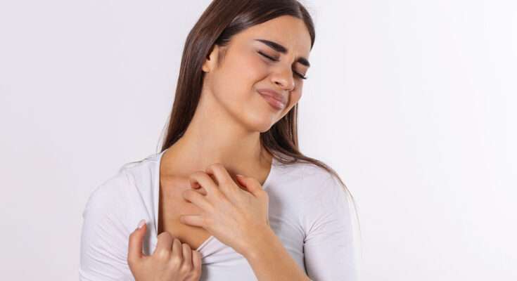 Donna con capelli castani e maglia chiara che si gratta il petto