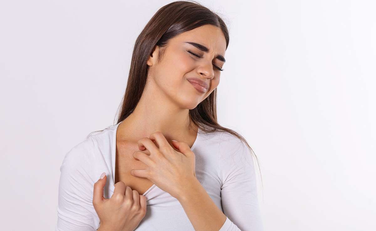 Donna con capelli castani e maglia chiara che si gratta il petto