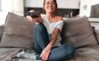 Donna seduta sul divano usa il telecomando per guardare serie TV