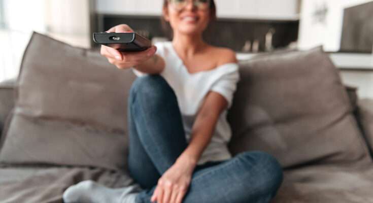 Donna seduta sul divano usa il telecomando per guardare serie TV